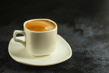 coffee in a white cup and coffee grain scattered on the table (freshly brewed hot drink with foam). food background. top