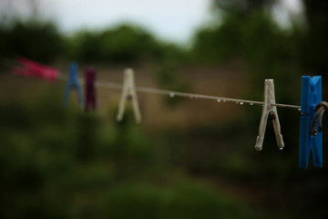 Fototapeta na wymiar Wet colorful pegs hanging on a clothesline after the rain in the backyard. No clothes outside, it’s time to use dryer.