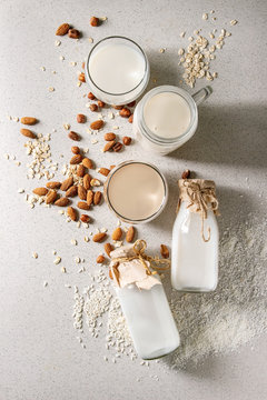 Variety of non-dairy vegan lactose free nuts and grain milk almond, hazelnut, coconut, rice, oat in glass bottles with ingredients above over white spotted background. Flat lay, space