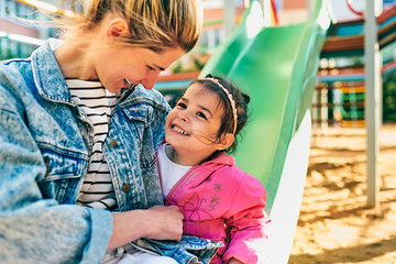 Candid outdoor portrait of happy little girl smiling and looking to her beautiful mother spending time together at playground. Young woman and daughter feeling happy, loving each other outside.