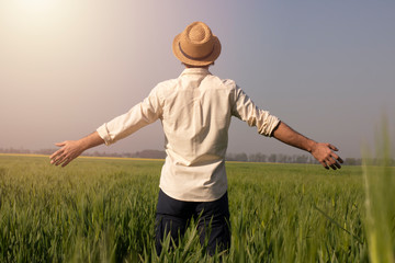 A successful man stands against the sun in a field of wheat. People in the open air amid nature with their hands up . The concept of freedom and discovery. Environment and way of life. Organic farming