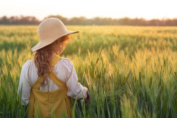 Obraz premium The child is a blonde curly-haired girl in a straw hat in a wheat field at sunset. Beautiful, romantic scene. The concept of organic farming and healthy lifestyle, healthy food. The concept of dreams,