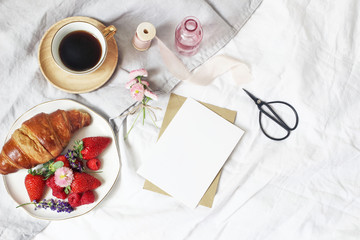 Obraz na płótnie Canvas Summer lifestyle composition. Blank greeting card mockup scene with cup of coffee, croissant pastry, strawberries, raspberries and daisy flowers. Breakfast in bed. Linen background. Flat lay, top view