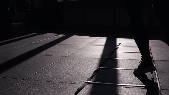 Woman in black leggings training at gym. Jumping from side to side on divided sections on the floor. Footage of determinated sportwoman training at gym with sunlight and shadows on the floor