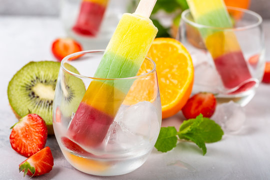 Striped popsicle with different flavors, mango, orange, kiwi and strawberry in glass cups. Summer food concept.