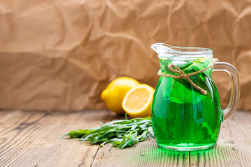 Summer cold green drink made from tarragon, with mint and slices lemon in glass decanter in focus...