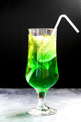 Summer cold green drink made from tarragon, with mint and slices lemon in glass with straw on black background. Sparkling beverage, lemonade. Horizontal with copy space