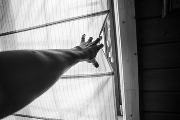 Black and white photo of male hand pulling back a curtain. Personal perspective view 