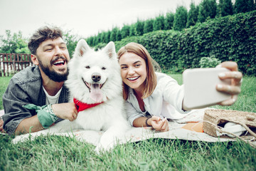 Beautiful couple spending time with a dog and taking selfie.