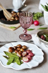young summer vegetables-fried radish, young peas and young potatoes. dinner served at the table, beautiful table setting.