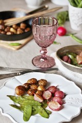 young summer vegetables-fried radish, young peas and young potatoes. dinner served at the table, beautiful table setting.