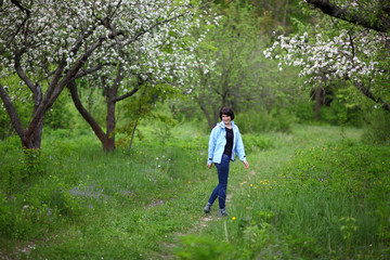 Beautiful mature woman posing for the camera in the spring garden. The girl enjoys the flowering of apple trees.