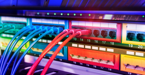 Server rack with blue and red internet patch cord cables connected to black patch panel in data...