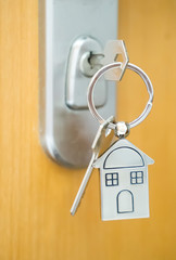 House key with home keyring in keyhole on wood door, copy space