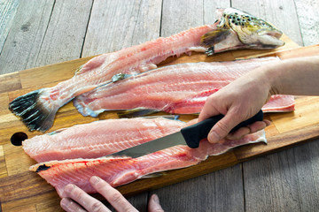 Filleting trout , removing rib bones with sharp fillet knife on wooden board - 267606476