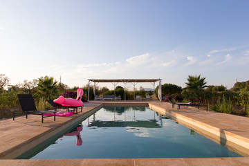 Empty sun beds near private pool and a pink flamingo while sunset.