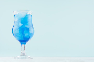 Blue beach cold alcohol drink with curacao liquor, ice cubes in elegant wineglass on pastel blue background and white wood table.