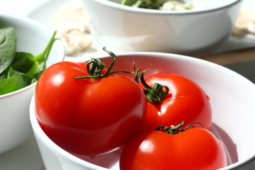 Fresh tomatoes in a white bowl, also some spinach and mushrooms in the background