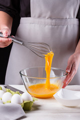 young woman in a gray aprons breaks the eggs