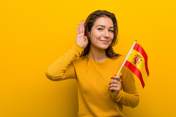 Young european woman holding a spanish flag trying to listening a gossip. - obrazy, fototapety, plakaty