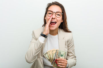 Young european business woman holding dollar banknotes shouting excited to front.