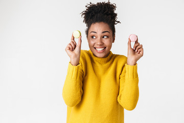 Young african excited emotional happy woman posing isolated over white wall background holding sweeties macaroons.
