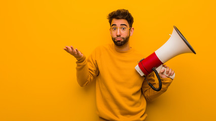 Young man holding a megaphone confused and doubtful