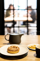 Gray teapot on a wooden table in a cafe. Black mug for tea. Dessert on a white plate and sliced lemon on a small saucer.