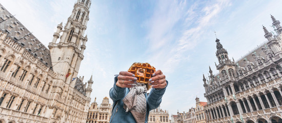 Fototapeta premium Young beautiful woman holding a traditional Belgian waffle on the background of the Great Market Square in Brussels, Belgium