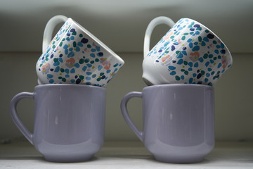 Two lilac and two white mugs are on the shelf in the kitchen. Close-up