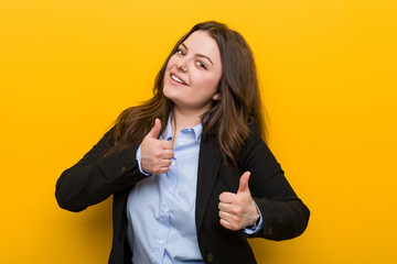 Young plus size caucasian business woman raising both thumbs up, smiling and confident.