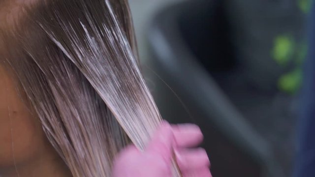 The hairdresser dyes the girl hair with special paint close up