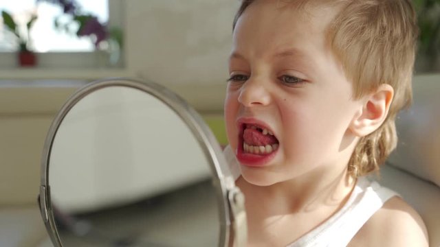 a small boy with blond hair with mirror opening his mouth to show where he lost one of his baby's teeth