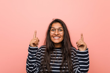 Young intellectual indian woman indicates with both fore fingers up showing a blank space.