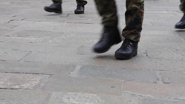 Close-up of military troops with military boots and camouflage trousers walking on stone pavement during a military parade. 