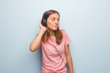 Naklejka premium Young pretty caucasian woman try to listening a gossip. She is listening to music with headphones.