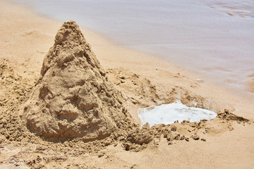 Sandy mountain with dug pit for water on shores of sea beach.