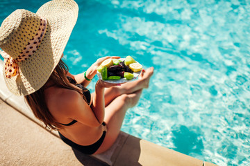 Woman in bikini eating fruits and relaxing in swimming pool. All inclusive. Summer vacation