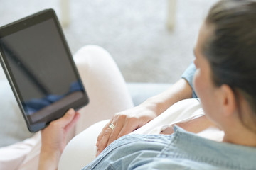 Pregnant woman using digital tablet, relaxing in couch