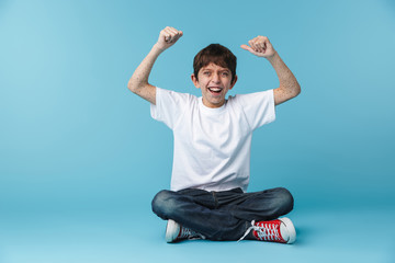 Image of happy brunette boy 10-12y with freckles wearing white casual t-shirt smiling at camera while sitting on floor