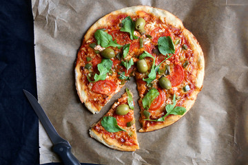 Homemade vegetarian pizza with tomato sauce, two types of cheese, tomatoes, peppers, arugula, olives and herbs. Top view.