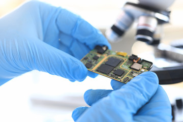 An employee of computer repair service assembly keeps spare part motherboard processor in hands gloves for installation by method soldering technology development