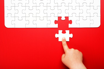Children's hand moves a piece of white puzzle on a red background