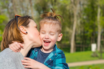 Mom kisses her little boy, who laughing in the park