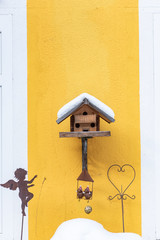 Homemade wooden bird's feeder in winter, under the snow on the yellow wall background.