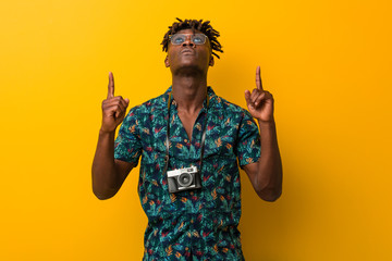 Young black rasta man wearing a vacation look pointing upside with opened mouth.