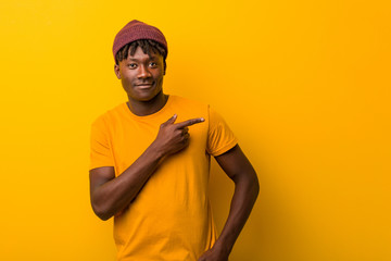 Young black man wearing rastas over yellow background smiling and pointing aside, showing something...