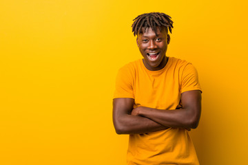 Young black man wearing rastas over yellow background laughing and having fun.