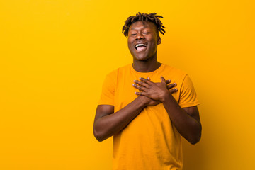Young black man wearing rastas over yellow background laughing keeping hands on heart, concept of happiness.