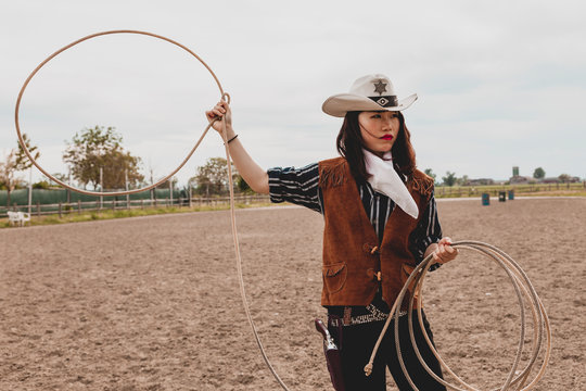 pretty Chinese cowgirl throwing the lasso in a horse paddock